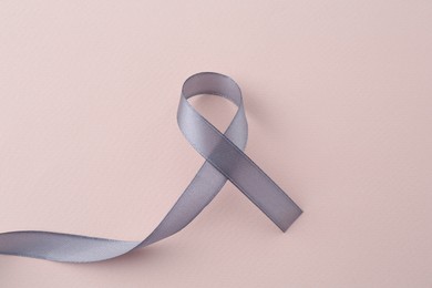Photo of Grey awareness ribbon on beige background, top view