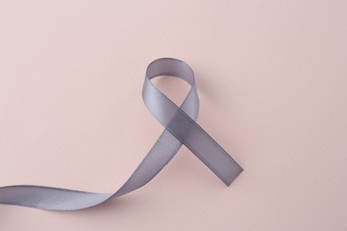 Grey awareness ribbon on beige background, top view