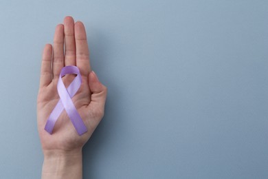 Woman with violet awareness ribbon on light blue background, top view. Space for text