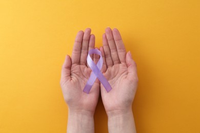 Woman with violet awareness ribbon on orange background, top view