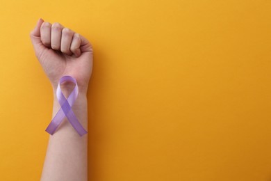 Woman with violet awareness ribbon on orange background, top view. Space for text