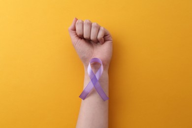 Woman with violet awareness ribbon on orange background, top view