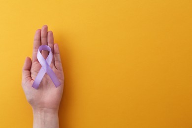 Woman with violet awareness ribbon on orange background, top view. Space for text