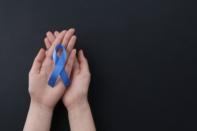 Woman with blue awareness ribbon on black background, top view. Space for text