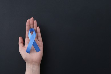 Woman with blue awareness ribbon on black background, top view. Space for text