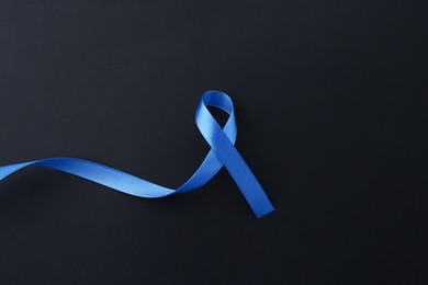 Photo of Blue awareness ribbon on black background, top view. Space for text
