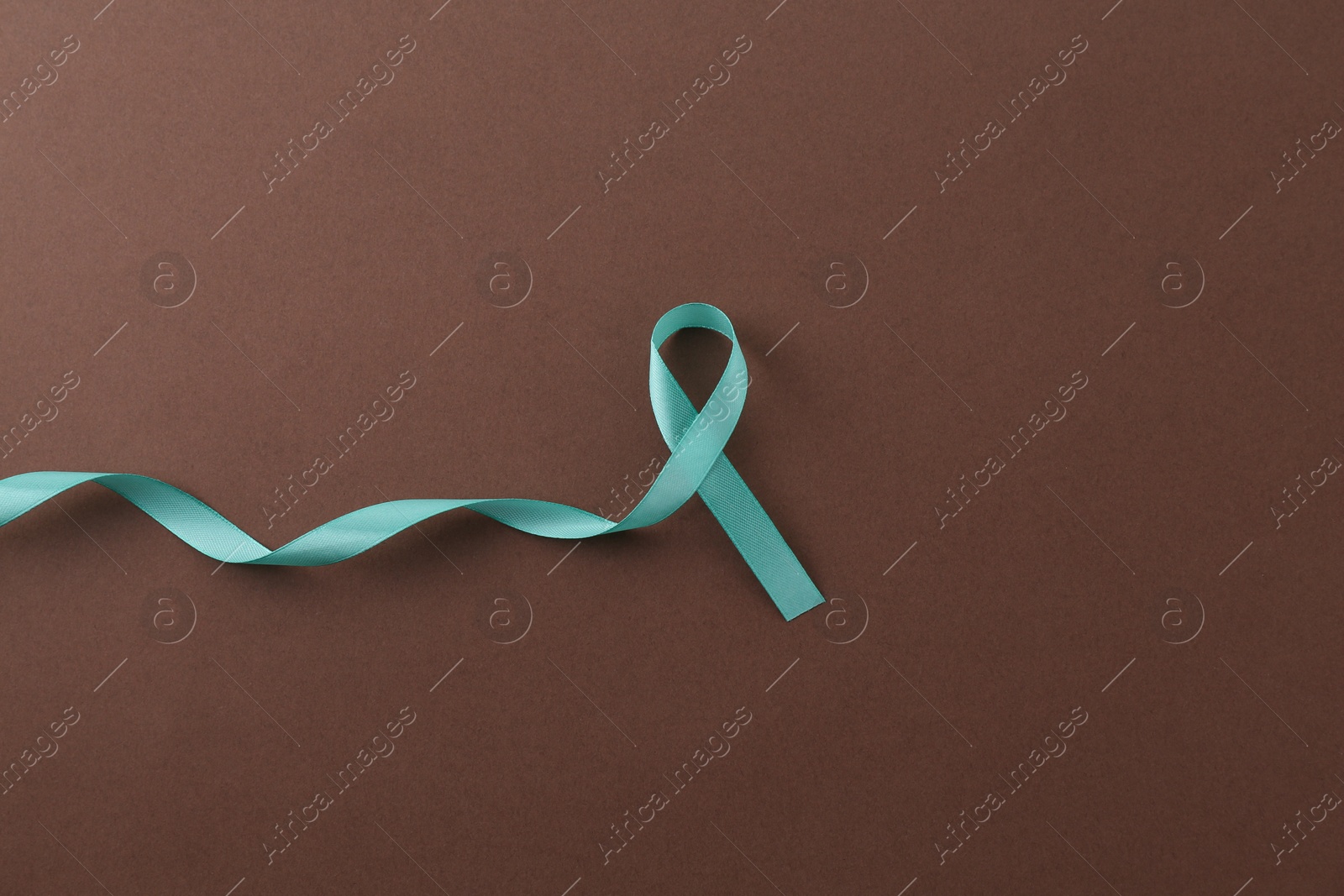 Photo of Turquoise awareness ribbon on brown background, top view. Space for text