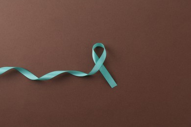 Photo of Turquoise awareness ribbon on brown background, top view. Space for text