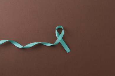 Turquoise awareness ribbon on brown background, top view. Space for text