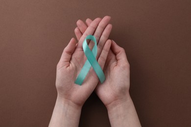 Photo of Woman holding turquoise awareness ribbon on brown background, top view