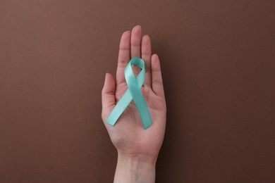 Photo of Woman holding turquoise awareness ribbon on brown background, top view