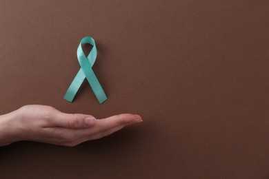 Woman with turquoise awareness ribbon on brown background, top view. Space for text