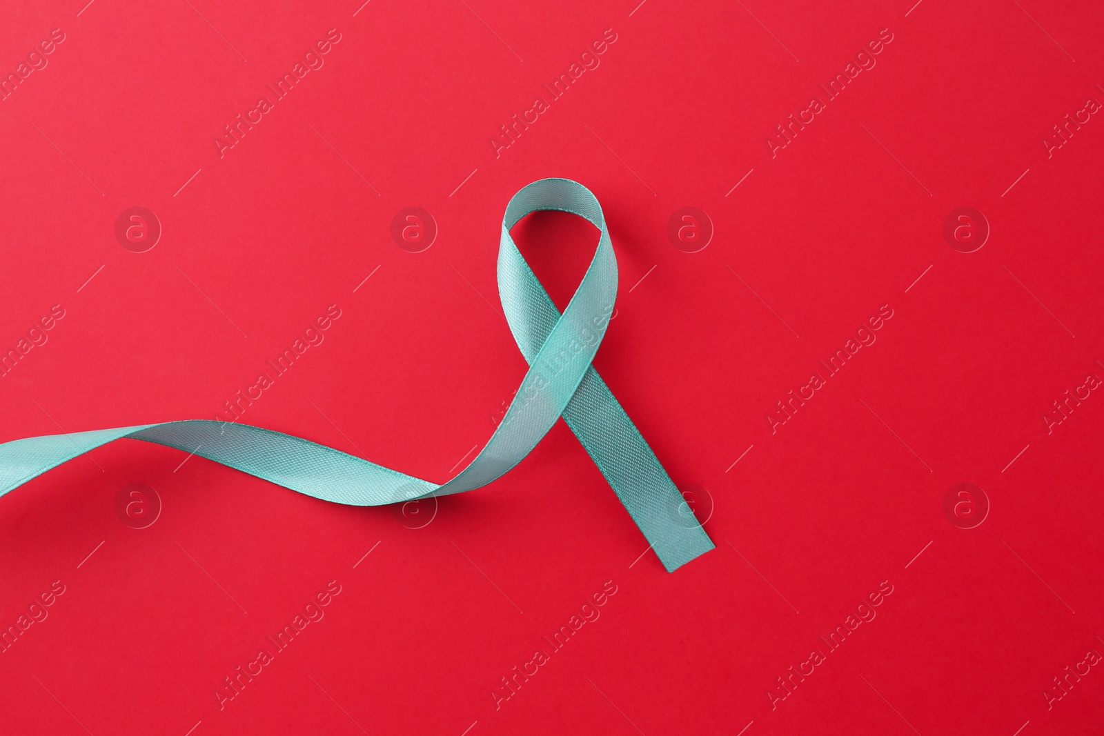 Photo of Turquoise awareness ribbon on red background, top view. Space for text