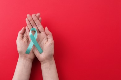 Photo of Woman holding turquoise awareness ribbon on red background, top view. Space for text