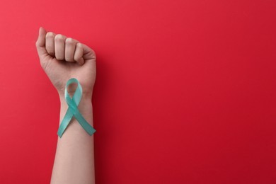 Woman holding turquoise awareness ribbon on red background, top view. Space for text