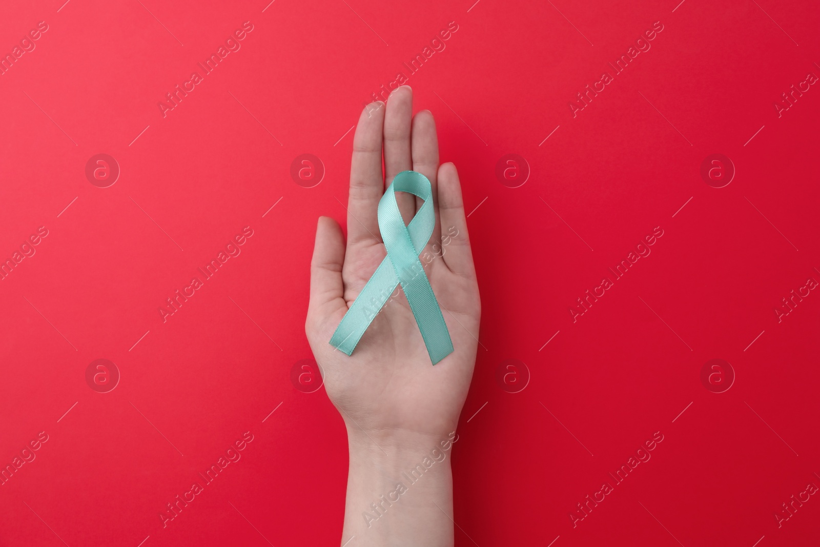 Photo of Woman holding turquoise awareness ribbon on red background, top view