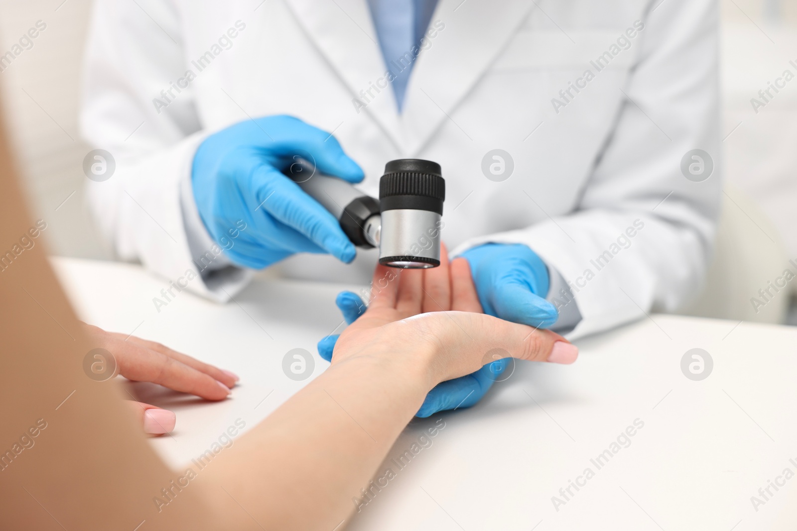 Photo of Dermatologist with dermatoscope examining patient at white table in clinic, closeup