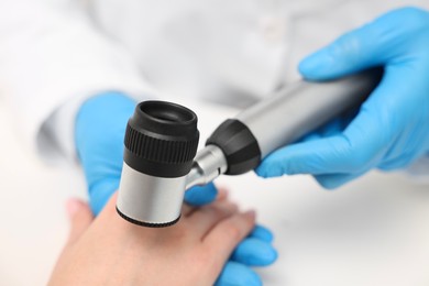 Photo of Dermatologist with dermatoscope examining patient at white table, closeup