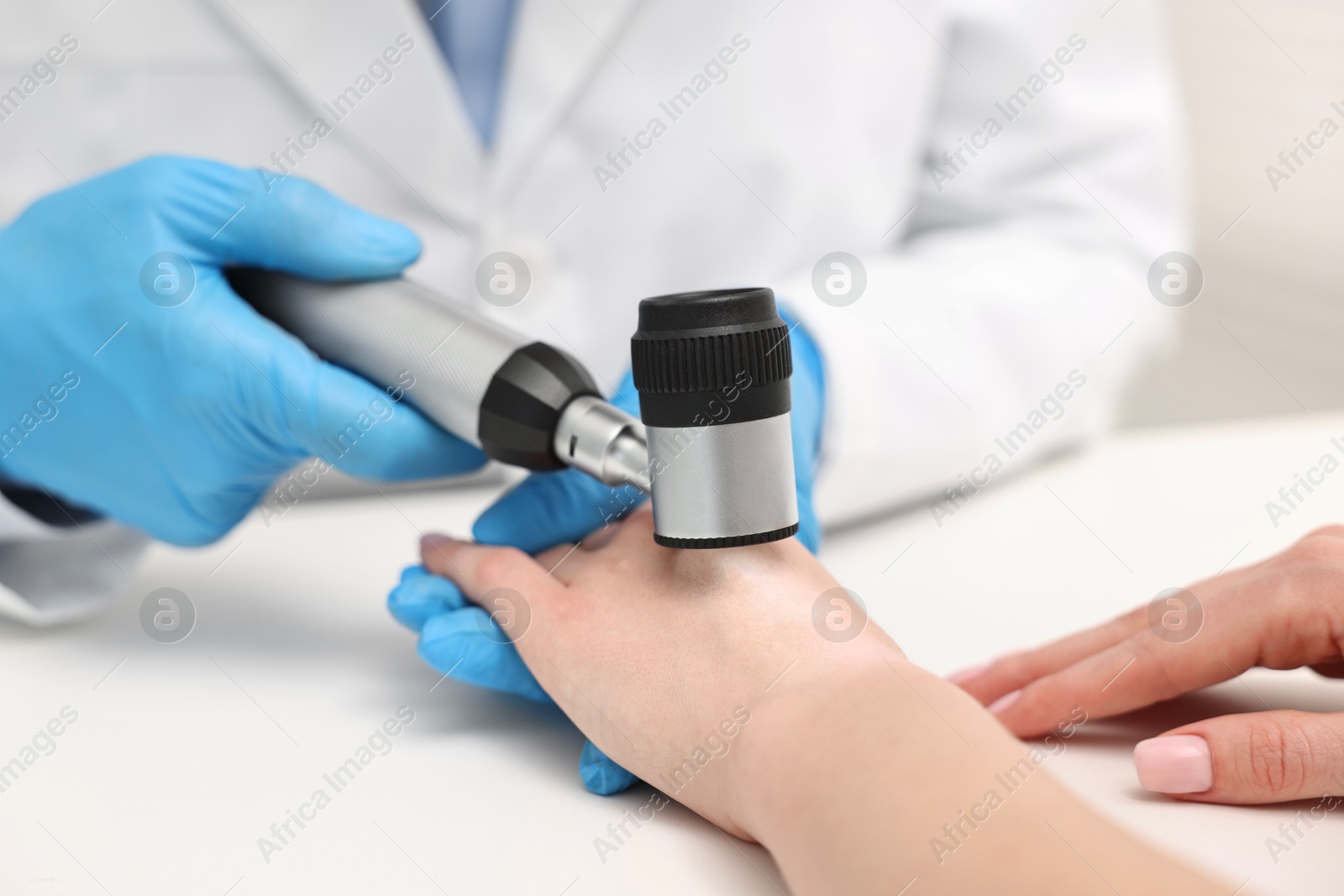 Photo of Dermatologist with dermatoscope examining patient at white table in clinic, closeup