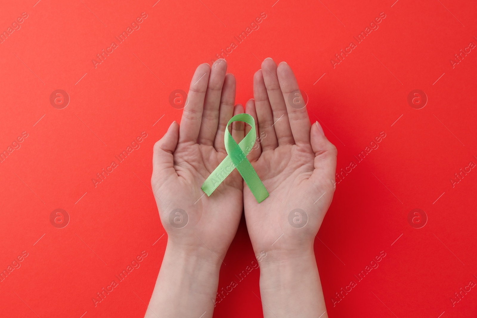 Photo of Woman with light green awareness ribbon on red background, top view