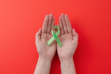 Photo of Woman with light green awareness ribbon on red background, top view