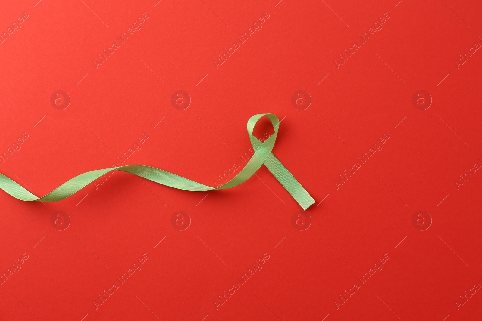 Photo of Light green awareness ribbon on red background, top view. Space for text