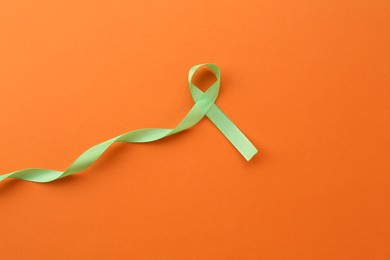 Photo of Light green awareness ribbon on orange background, top view