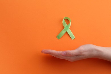 Woman with light green awareness ribbon on orange background, top view. Space for text