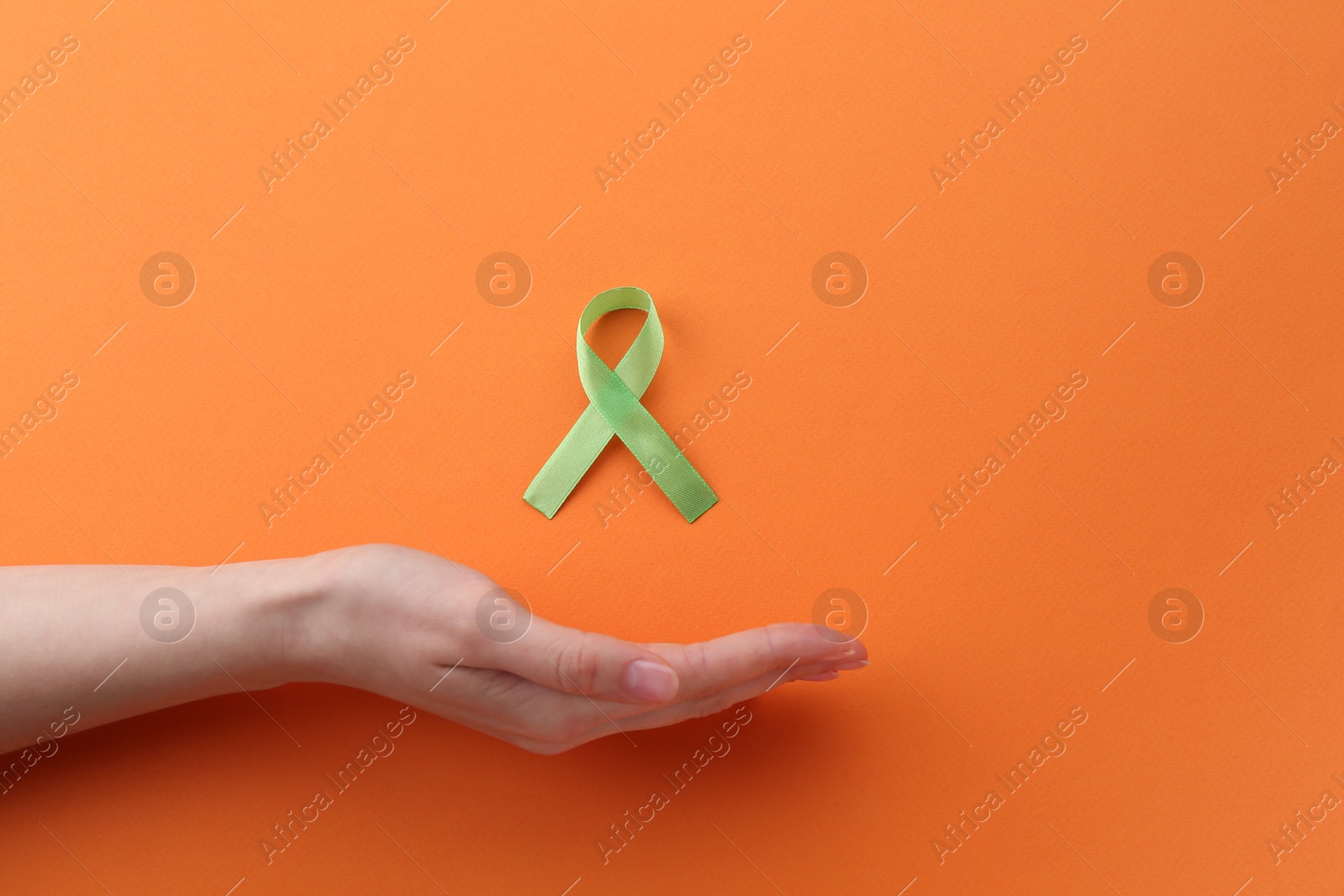 Photo of Woman with green awareness ribbon on orange background, top view. Space for text