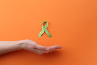 Woman with green awareness ribbon on orange background, top view. Space for text
