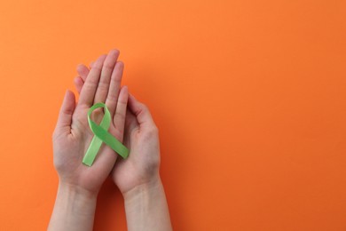 Woman with green awareness ribbon on orange background, top view. Space for text