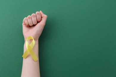 Photo of Woman with yellow awareness ribbon on green background, top view. Space for text