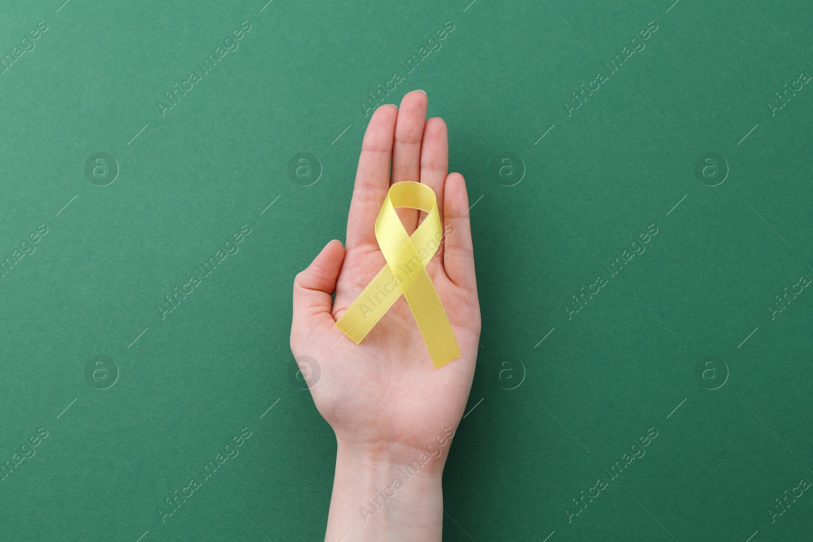 Photo of Woman with yellow awareness ribbon on green background, top view