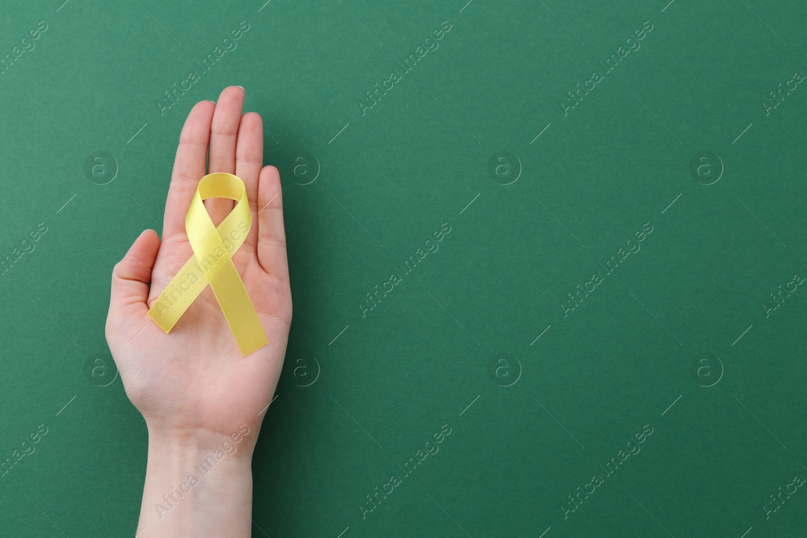 Photo of Woman with yellow awareness ribbon on green background, top view. Space for text