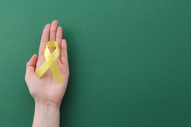 Woman with yellow awareness ribbon on green background, top view. Space for text
