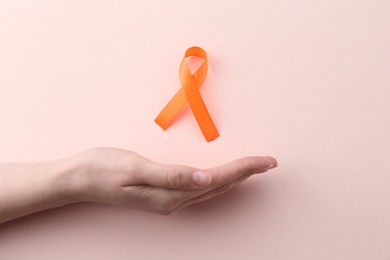 Woman with orange awareness ribbon on beige background, top view