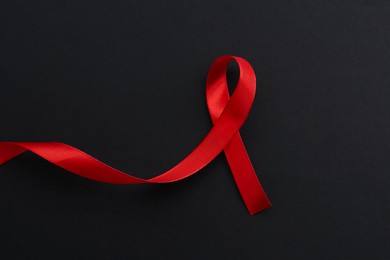 Photo of Red awareness ribbon on black background, top view