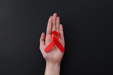 Photo of Woman with red awareness ribbon on black background, top view