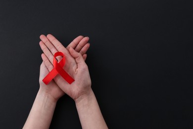 Photo of Woman with red awareness ribbon on black background, top view. Space for text