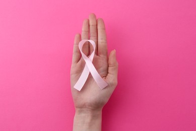 Photo of Woman with awareness ribbon on pink background, top view