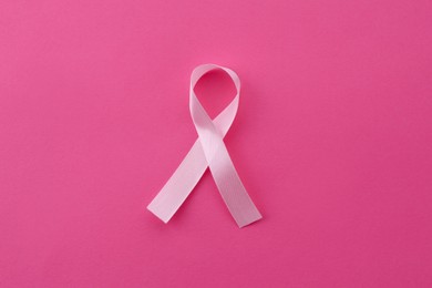 Awareness ribbon on pink background, top view