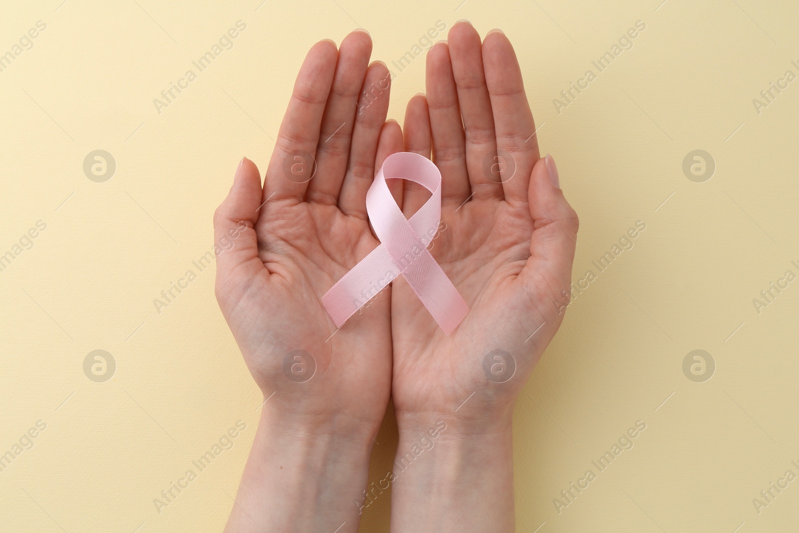 Photo of Woman with pink awareness ribbon on pale yellow background, top view