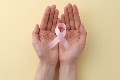 Woman with pink awareness ribbon on pale yellow background, top view