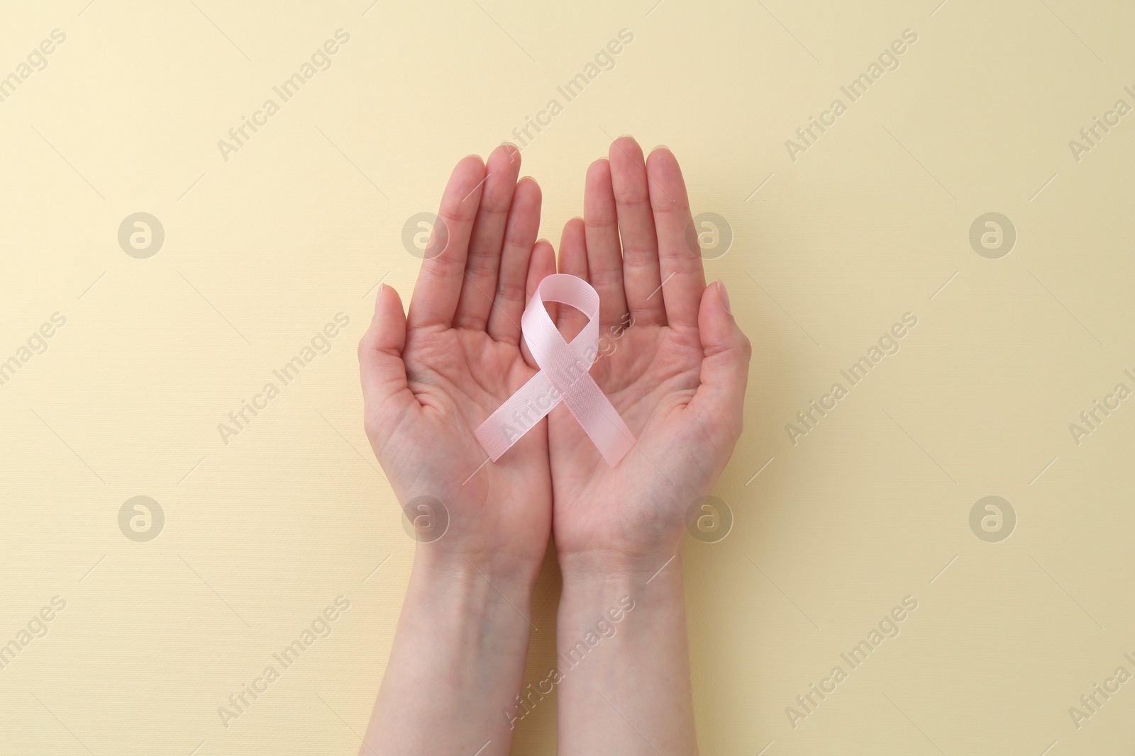 Photo of Woman with pink awareness ribbon on pale yellow background, top view