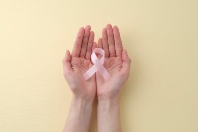 Woman with pink awareness ribbon on pale yellow background, top view