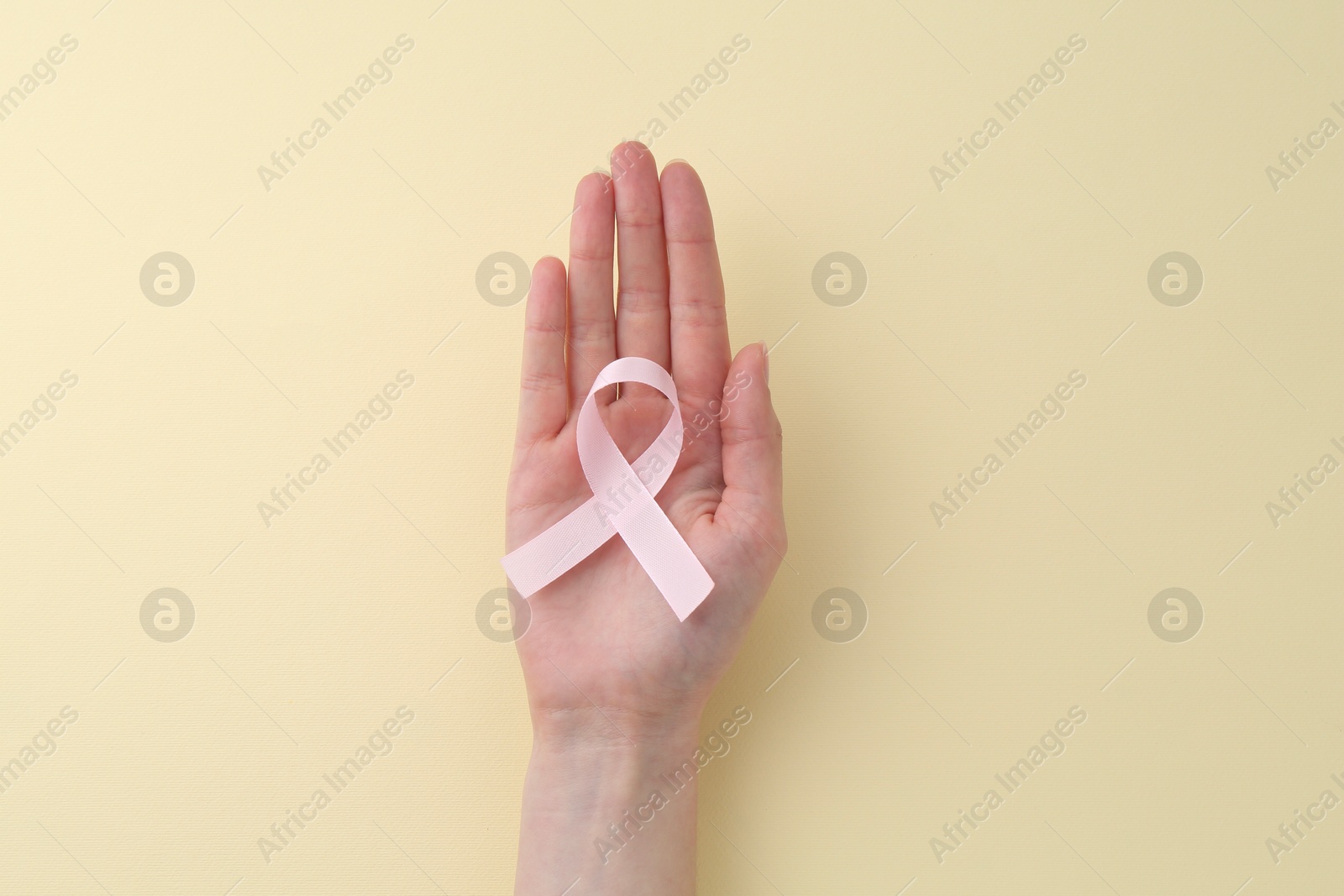 Photo of Woman with pink awareness ribbon on pale yellow background, top view