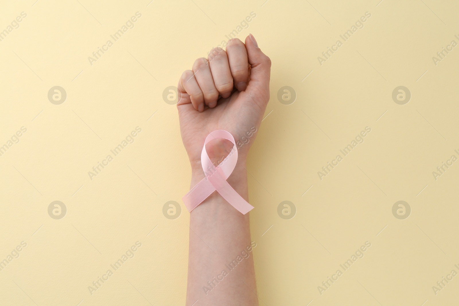 Photo of Woman with pink awareness ribbon on pale yellow background, top view