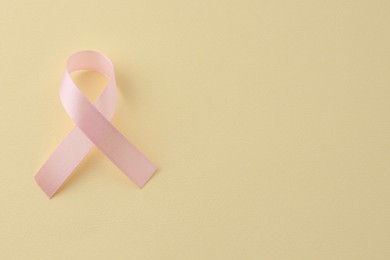Photo of Pink awareness ribbon on pale yellow background, top view