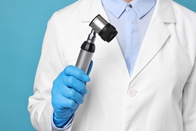 Dermatologist with dermatoscope on light blue background, closeup