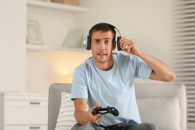 Surprised man in headphones playing video games with joystick at home